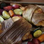 Corn husk-wrapped chicken and roasted veggies at an low angle