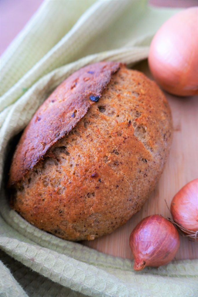 Oblique shot of an onion sourdough with a green towel and 3 onions