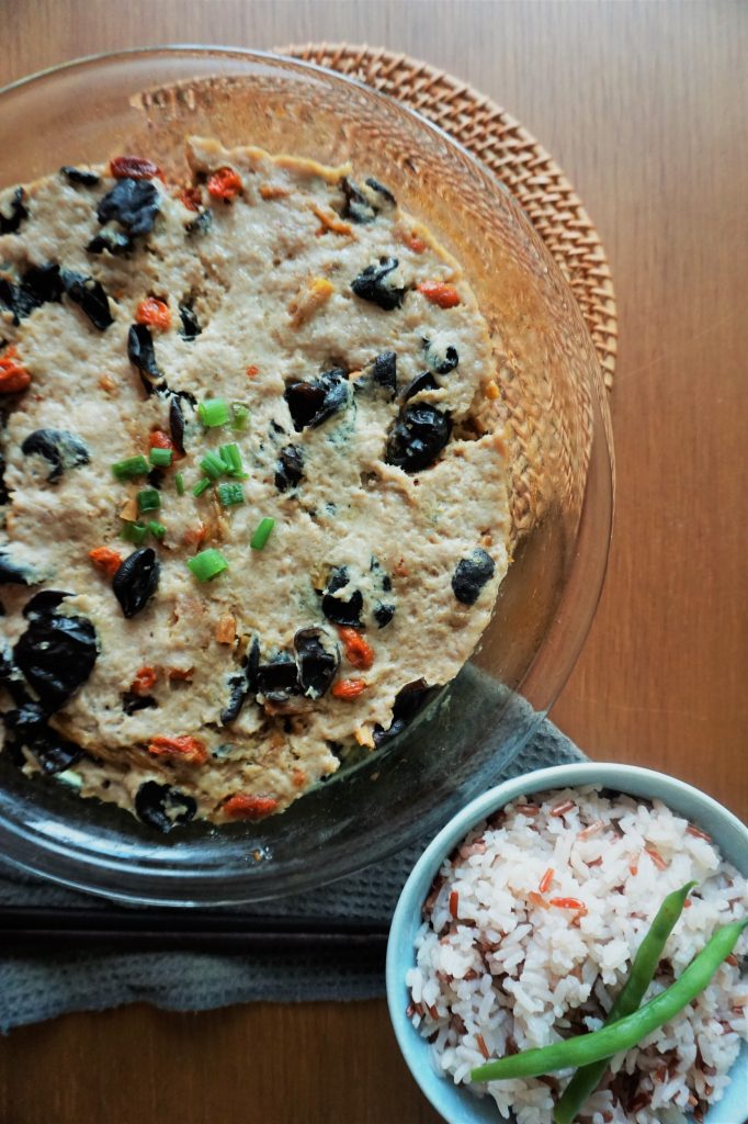 Steam meat patty with black fungus in glass dish with a bowl of rice and a couple green beans on top