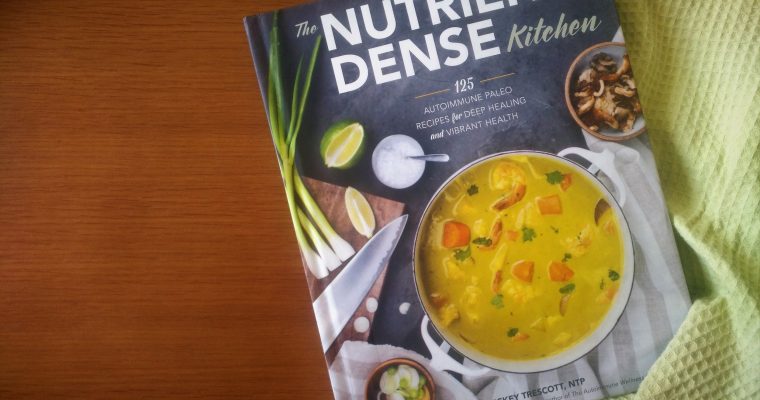 The Nutrient-Dense Kitchen book on a wood-patterned table with a green dish cloth spread next to it